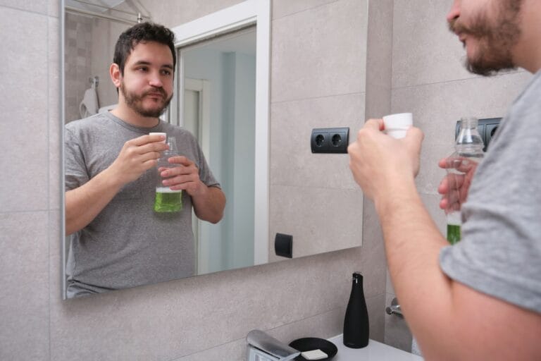 Shocking Misconceptions About Oral Health You Need to Know Man rinsing mouth with green mouthwash in bathroom. Teeth care concept.