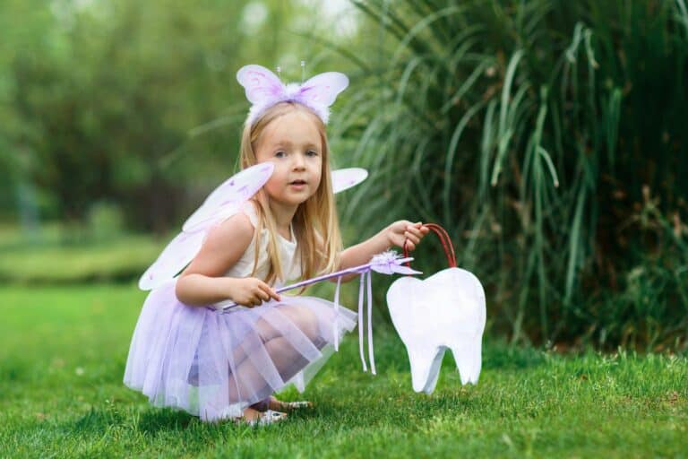 What’s the Story Behind the Tooth Fairy? Little girl with blonde hair wearing fairy tooth costume outdoor at summer